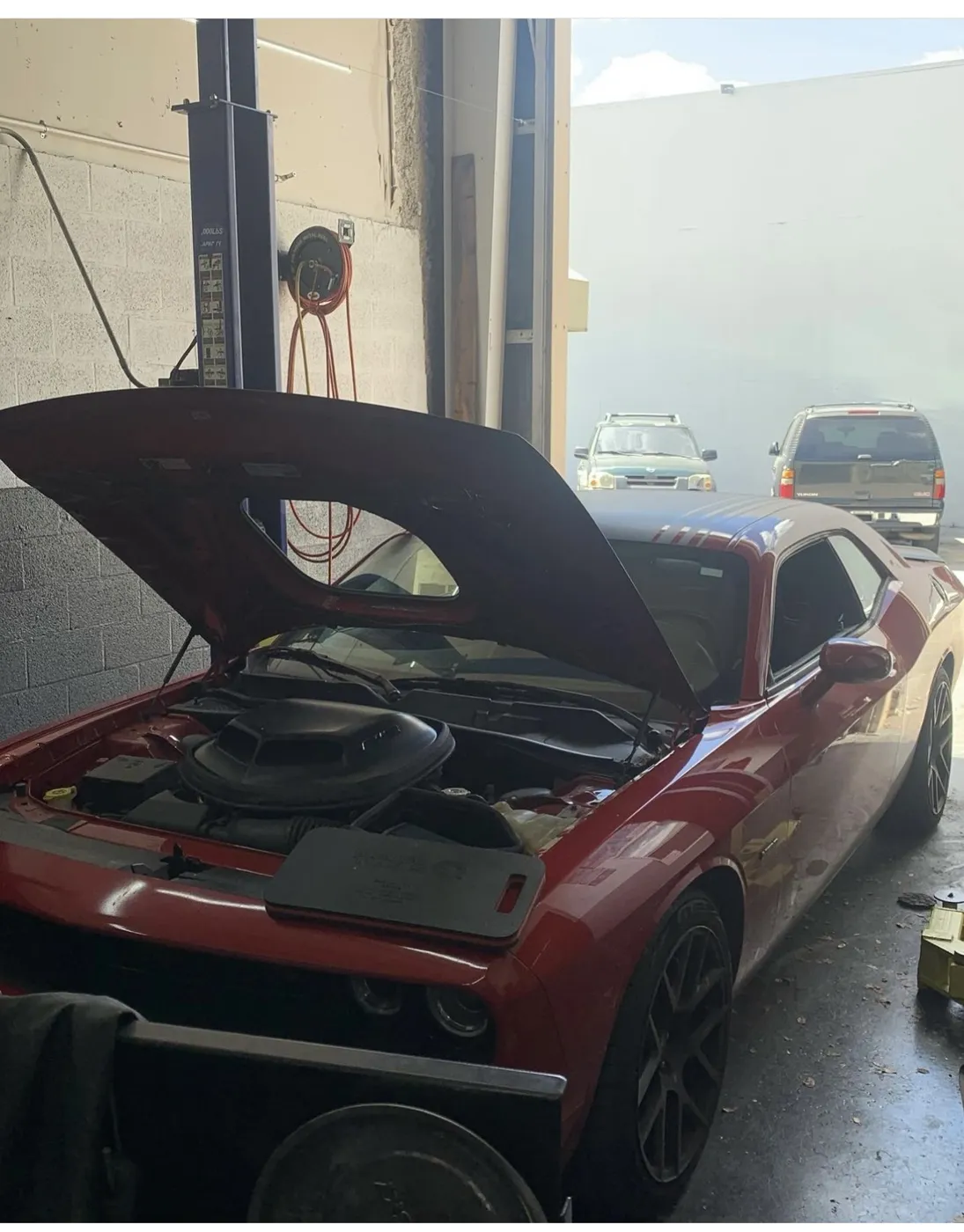 A red muscle car with the hood up in the bay